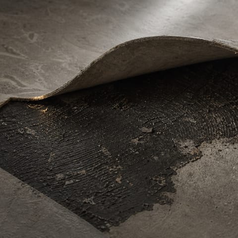 Svart limrester under en uppfläkt golvmatta på betonggolv